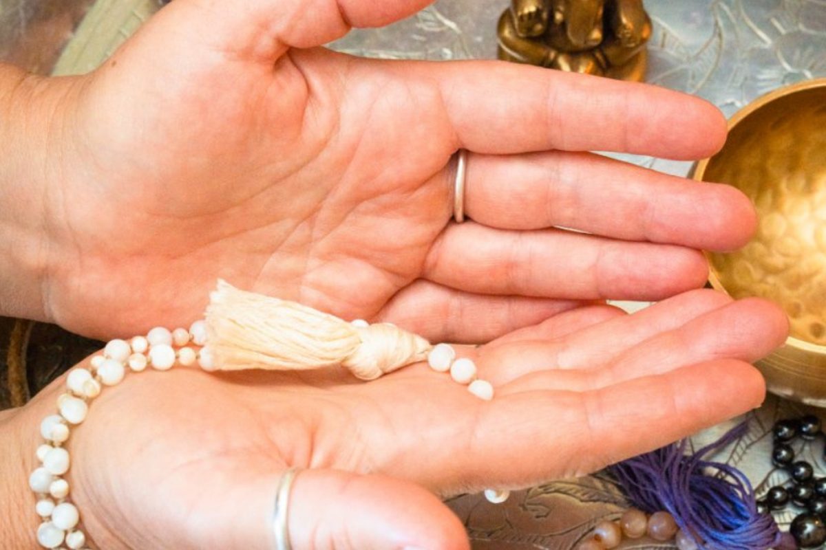 Open hands holding mala beads beside a singing bowl