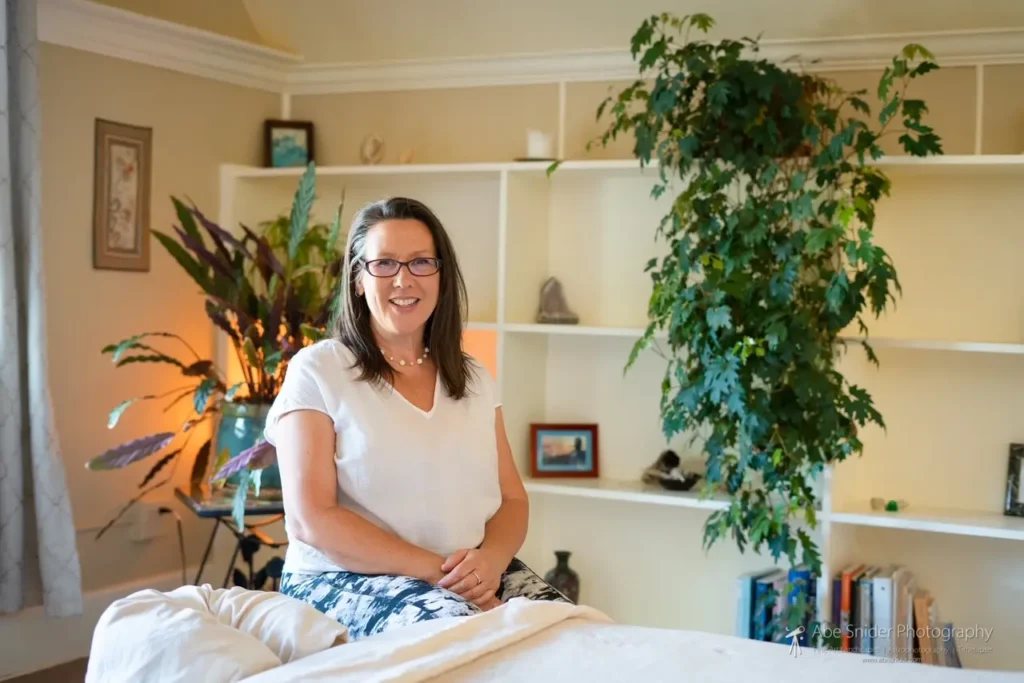 Aileen seated at her massage table in the treatment room